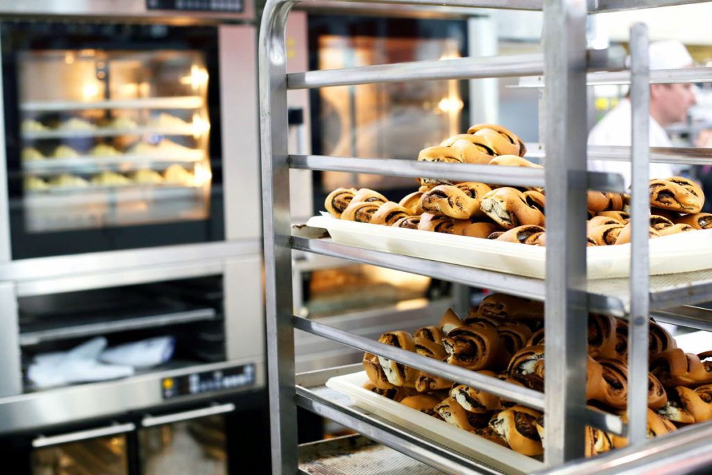 Commercial kitchen showing a baking rack with some sweets and a commercial baking oven on the background.