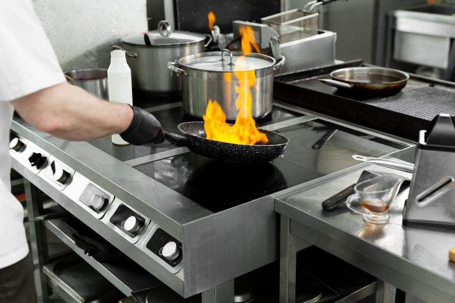 a chef prepares food at a commercial range with a flaming frying pan