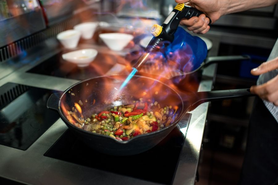 a chef uses a blowtorch to sear food at a commercial range