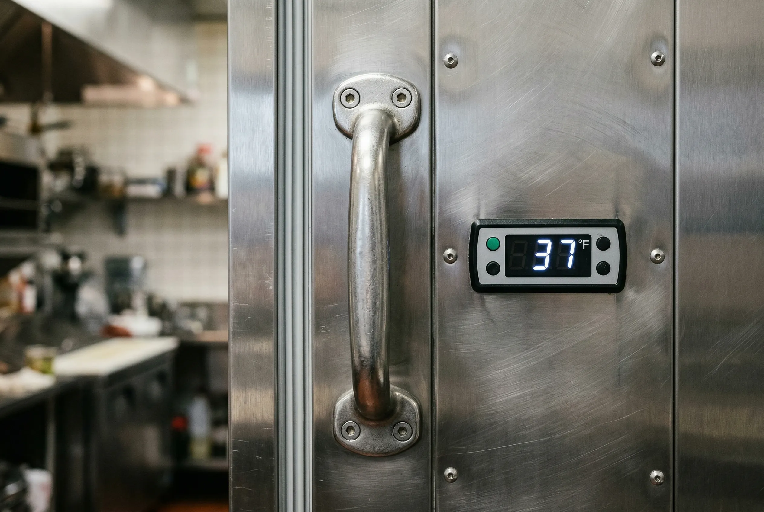 Close-up detail of a stainless steel commercial reach-in refrigerator door handle and temperature display